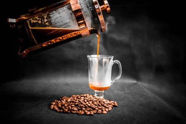 French press pouring black coffee in an Irish coffee mug, coffee beans next to the mug, black background (1)