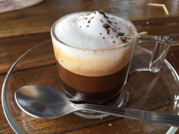 A glass of cappuccino with 3 distinct layers - coffee, steamed milk, and foamed milk