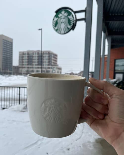 Closeup of person's hand holding a Blonde Vanilla Latte in a Starbucks branded mug