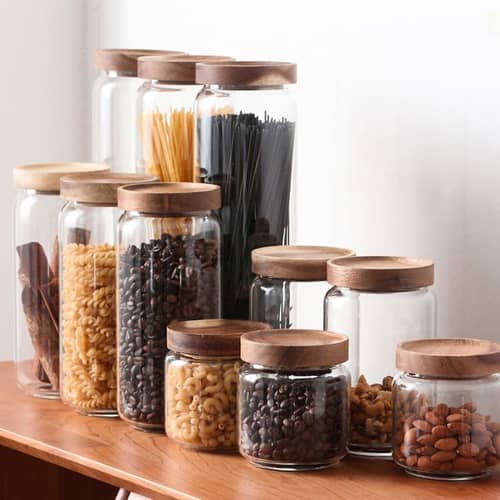 Freshly roasted coffee beans in  glass jar storage among other food items on a wooden kitchen shelf
