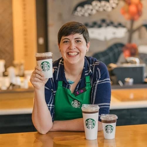  Starbucks barista smiling and holding branded drinks cups