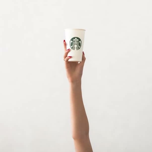Shot of person's hand holding a Starbuck Coffee branded paper cup up high