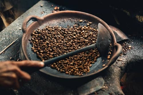 Closeup of unidentified Asian traditionally roasting coffee beans over a charcoal fire
