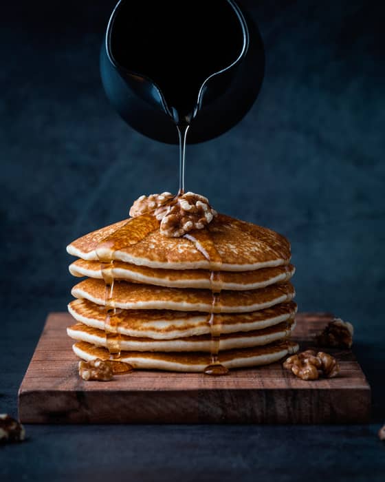 Rich syrup pouring onto a stack of buttery pancakes