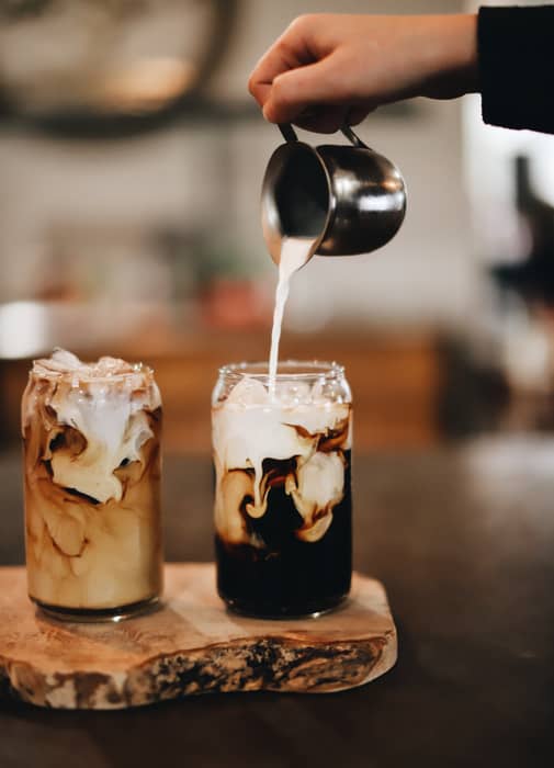 Person is pouring milk into two glasses of cold brew coffee 