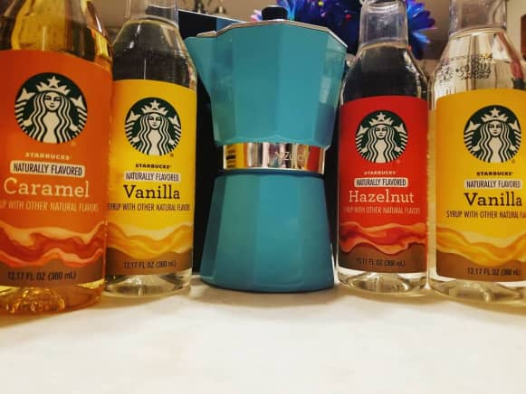  Starbucks sauce vs syrup: A selection of Starbucks syrups next to a baby blue Italian-style Moka pot on a table ready for home use
