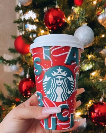 Person holding a Peppermint Mocha in front of a Christmas tree