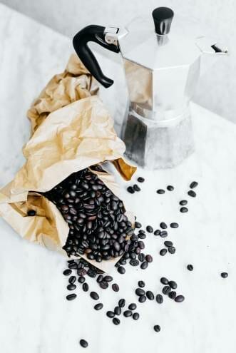 Very dark brown (imminent) coffee beans in a bag next to a Moka pot