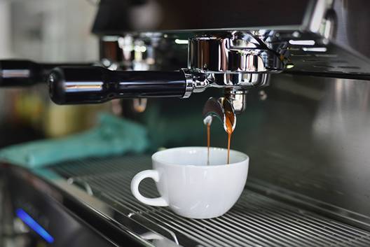 An espresso machine filling a white ceramic mug with coffee