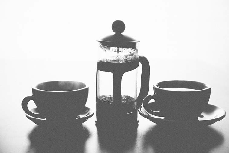 Two ceramic mugs beside a French press with a black and white background