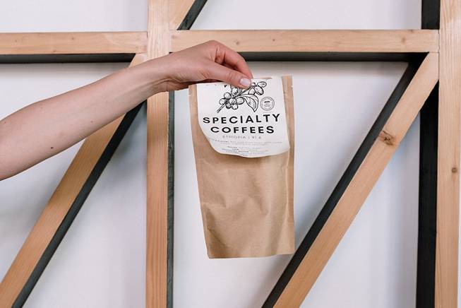 A hand of a person holding a brown packaging bag written Specialty Coffees