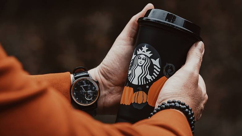 Hands of a person holding a black and white Starbucks cup