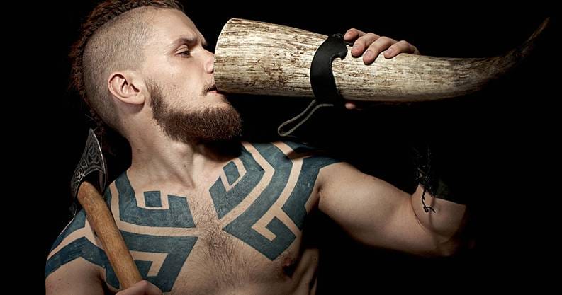 A man with tattoos drinking from a large horn.