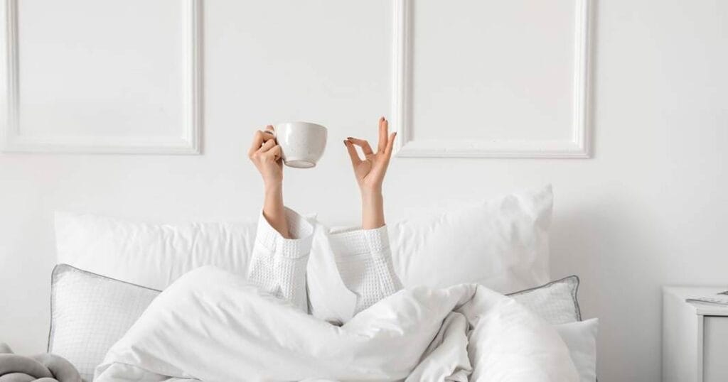 A woman laying in bed with a cup of coffee.