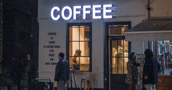 People walk past a coffee shop on a snowy night.