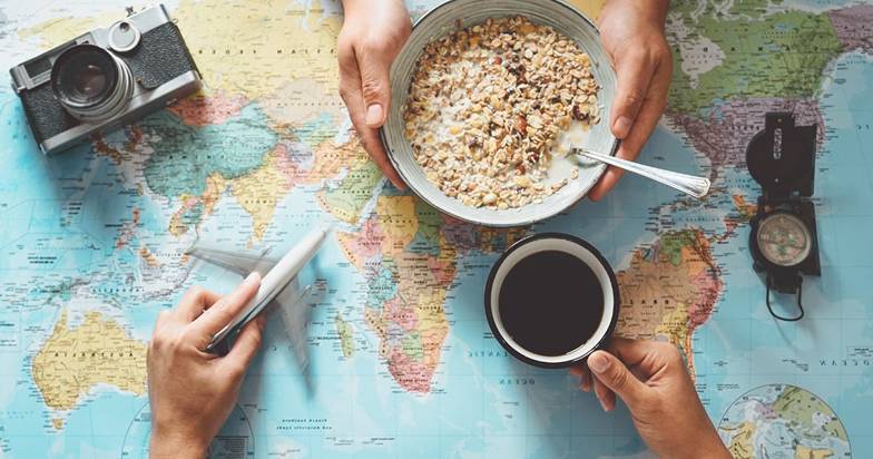 Hands holding a bowl of cereal and coffee on a world map.