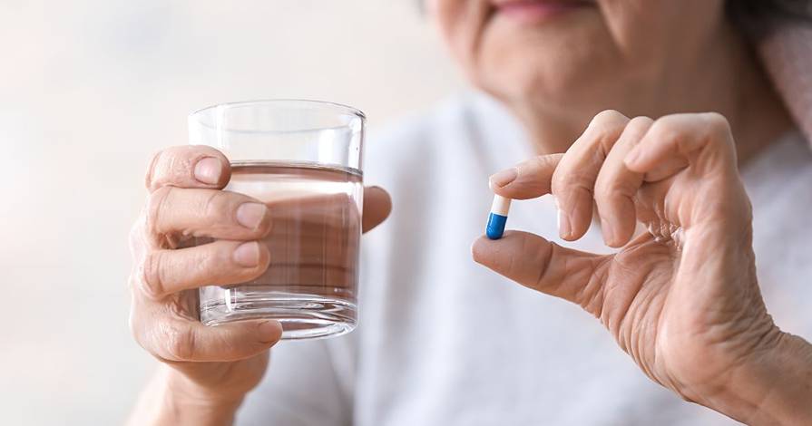 A woman holding a pill and a glass of water.