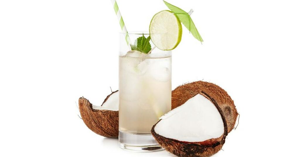 A coconut drink with lime and ice in a glass on a white background.
