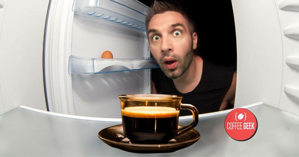 A man is standing in front of a refrigerator with a cup of coffee.