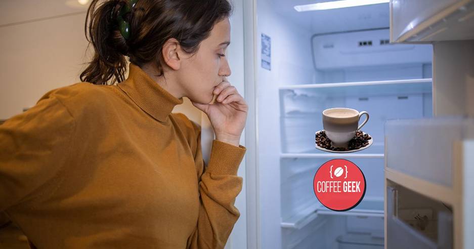 A woman is looking at a cup of coffee in an open refrigerator.