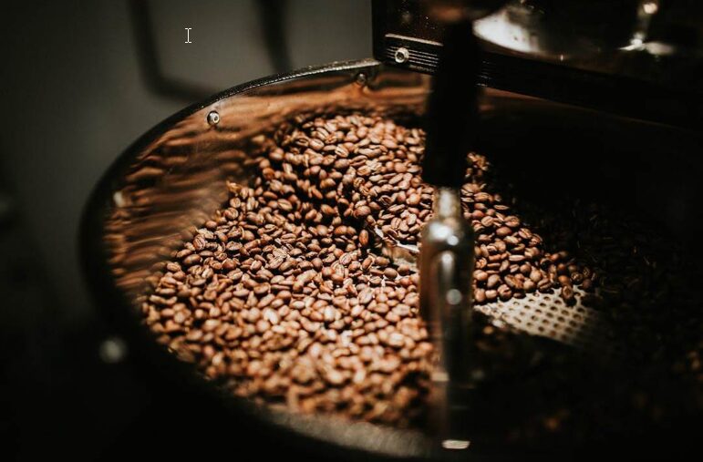 Close-up of coffee beans roasting inside a metal drum roaster, with a metal arm visible among the beans.